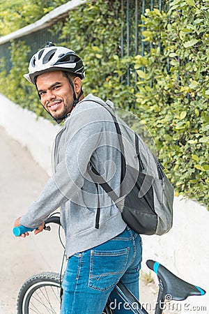 Young black man sitting on a bike in a park, leaning on the handlebars smiling, side view Stock Photo