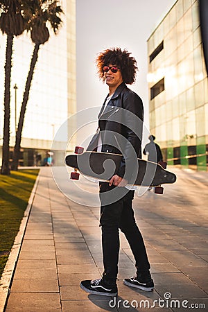 Young black man with skateboard walking in street and looking Stock Photo