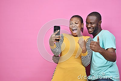 young black man and woman feeling excited and happy viewing content on a mobile phone together, giving thumbs up gesture Stock Photo