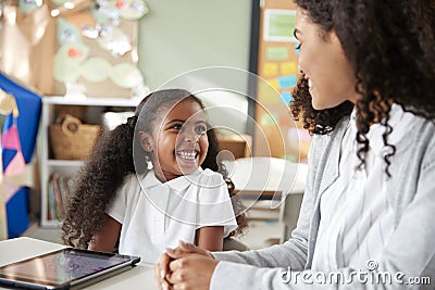 Young black schoolgirl sitting at a table with a tablet computer in an infant school classroom learning one on one with female tea Stock Photo