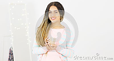 Young black woman with afro hairstyle smiling. Girl with cup hot drink wearing pink dress. Studio shot Stock Photo