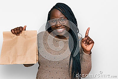 Young black woman with braids holding take away paper bag surprised with an idea or question pointing finger with happy face, Stock Photo