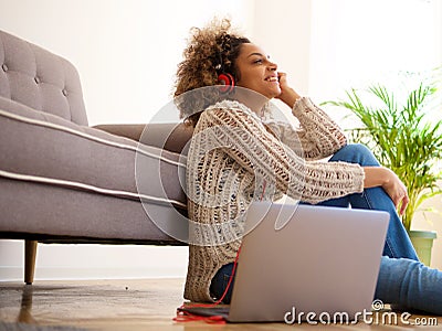 Young black woman sitting on the floor at home and listening to music with laptop and headphones Stock Photo