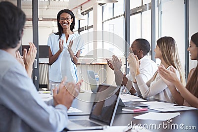 Young black woman stands clapping with colleagues at meeting Stock Photo