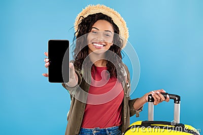 Young black woman with suitcase showing smartphone at camera, offering mockup, booking summer vacation online Stock Photo