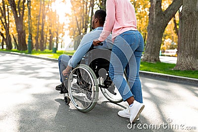 Young black woman taking her paraplegic boyfriend in wheelchair for walk at urban park in autumn Stock Photo