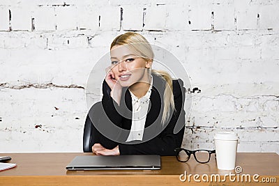 Young blond beauty businesswoman sitting at a office table with laptop, notebook and glasses in suit. Business concept. Stock Photo