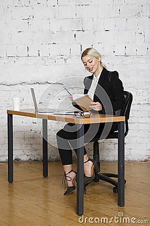 Young blond beauty businesswoman sitting at a office table with laptop, notebook and glasses in suit. Business concept. Stock Photo