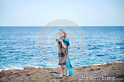 Young blond girl in a fairy-tale dress like a bird holding a royal crown strolling along the shore Stock Photo