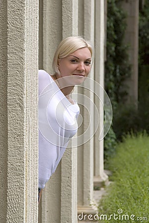 Young blond girl looks out from behind a column Stock Photo