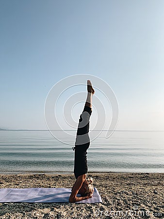 Young blond girl practice yoga headstand asana on sea shore at sunrise Stock Photo