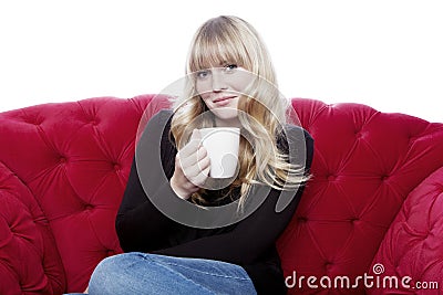 Young blond haired girl drink cup of coffee on red sofa in front Stock Photo