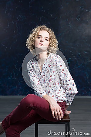 A young blond handsome man androgyn in the image of an attractive woman posing sitting on a chair Stock Photo