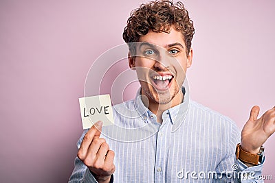Young blond romantic man with curly hair holdiing paper with love message for valentines day very happy and excited, winner Stock Photo