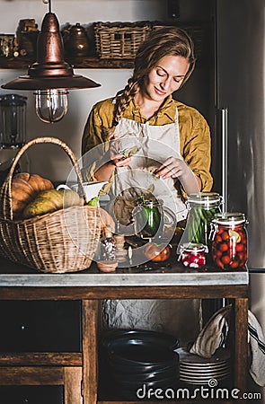 Young blond woman in linen apron making homemade vegetable preserves Stock Photo