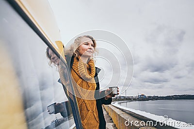 Young blond woman looking out of camper van overlooking the sea Stock Photo