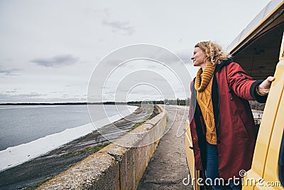 Young blond woman looking out of camper van overlooking the sea Stock Photo