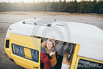 Young blond woman looking out of camper van with solar panel on the roof top and pine forest on the background Stock Photo