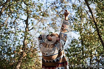 Young blond woman, wearing colorful cardigan, stretching her arms up to the sun in park in autumn. Close-up picture of girl from Stock Photo