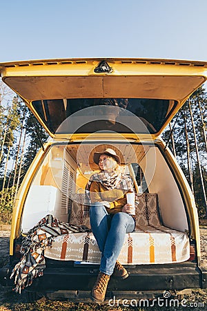 Young blonde Caucasian woman relaxing in her campervan at sunset Stock Photo