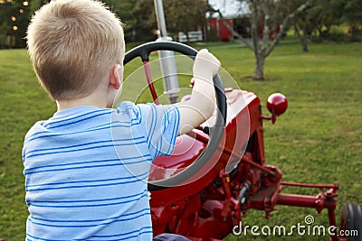 Young Blonde child pretending to drive an antique red tractor in Stock Photo