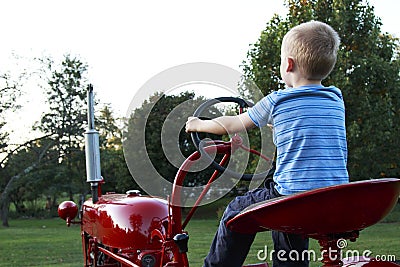 Young blonde child pretending to drive an old red tractor to the Stock Photo