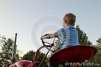 Young Blonde child pretending to drive a red tractor Stock Photo