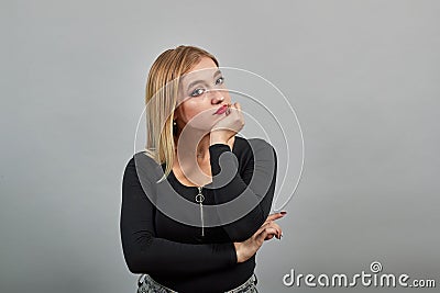 Young blonde girl in black jacket young woman thinks, holds her hand on chin Stock Photo