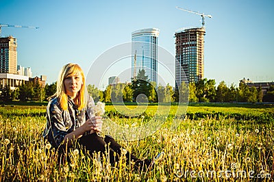 Young blonde girl in dress with shoulder bag, walking on dandelion field Stock Photo