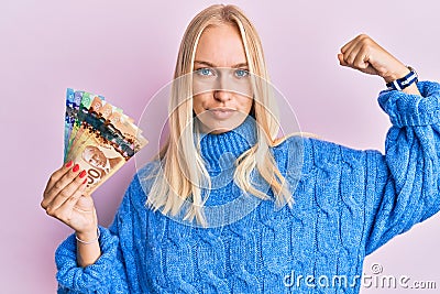 Young blonde girl holding canadian dollars strong person showing arm muscle, confident and proud of power Stock Photo