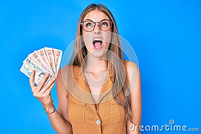 Young blonde girl holding united kingdom pounds angry and mad screaming frustrated and furious, shouting with anger looking up Editorial Stock Photo