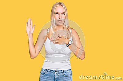 Young blonde girl wearing casual style with sleeveless shirt swearing with hand on chest and open palm, making a loyalty promise Stock Photo