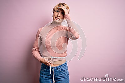 Young blonde thin woman with short hair measuring body figure using measure tape stressed with hand on head, shocked with shame Stock Photo