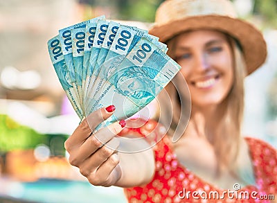 Young blonde tourist woman wearing summer style holding brazilian 100 real banknotes at the city Stock Photo