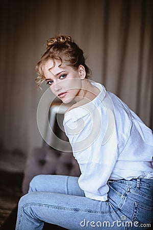 Young blonde woman in a casual white shirt and jeans in a loft interior, close up fashion portrait Stock Photo