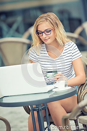 Young blonde woman holding credit card and using laptop computeron the terrace of the caf Stock Photo