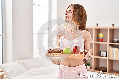 Young blonde woman holding healthy breakfast smiling at bedroom Stock Photo