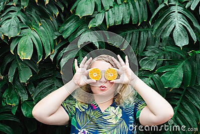 Young blonde woman holding slices of orange tangerine in front of her eyes, kissing Stock Photo