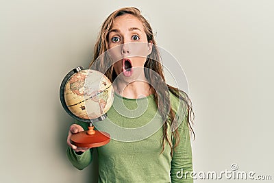 Young blonde woman holding vintage world ball scared and amazed with open mouth for surprise, disbelief face Stock Photo