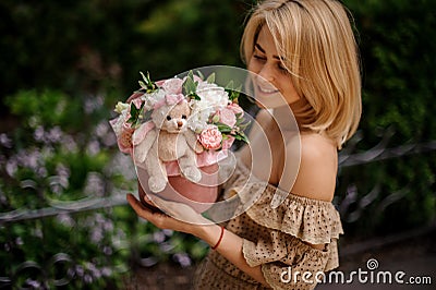 Young blonde woman holds cute round box with flowers decorated with soft toy Stock Photo
