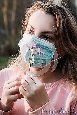 A young blonde woman inhales the smell of a flower through a medical mask Stock Photo