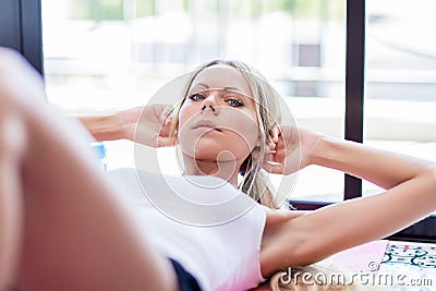 Young blonde woman makes abdominal sit-ups exercise on mat at ho Stock Photo