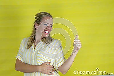 Young blonde woman over isolated background smiling with happy face looking and pointing to the side with thumb up Stock Photo