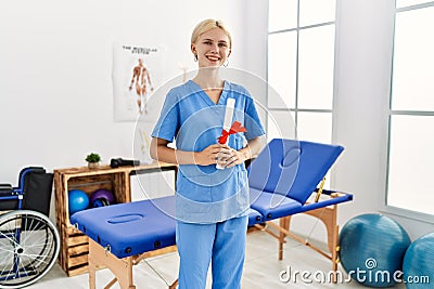 Young blonde woman physiotherapist smiling confident holding diploma at rehab clinic Stock Photo