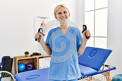 Young blonde woman physiotherapist smiling confident holding press hand tool at rehab clinic Stock Photo