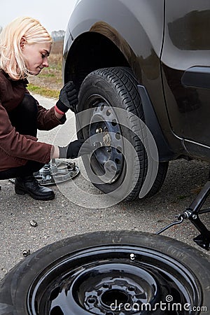 A young blonde woman removes the wheel with a key near her car with a flat tire Stock Photo