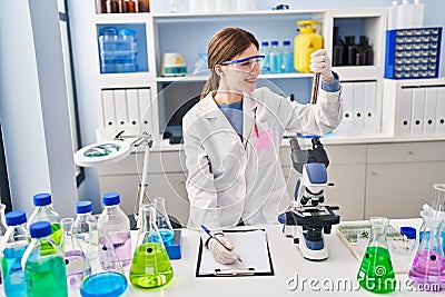 Young blonde woman scientist analysing test tube writing on clipboard at laboratory Stock Photo