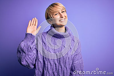 Young blonde woman with short hair wearing winter turtleneck sweater over purple background Waiving saying hello happy and Stock Photo