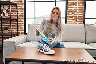 Young blonde woman smiling confident holding insole shoe at home Stock Photo