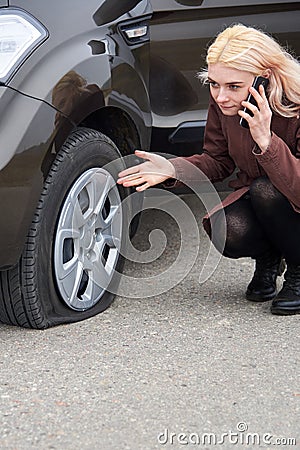 A young blonde woman talking on a mobile phone near her car with a flat tire Stock Photo